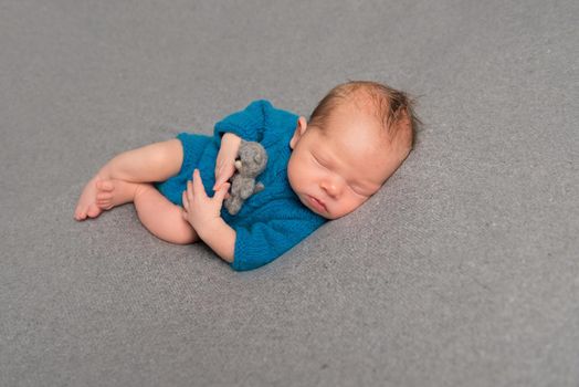 Tired baby in a blue costume napping after a tough day, hugging a teddy