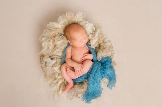 Lovely newborn sleeping on a knitted blue scarf in a basket for kids, topview