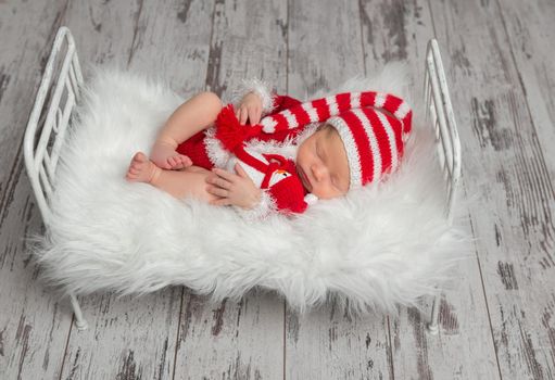 Sweet baby wearing Santa's costume hugging a toy of a snowman in his sleep