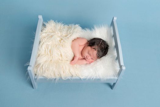 Tranquil infant sleeping on his side, covering himself with a white blanket, closeup