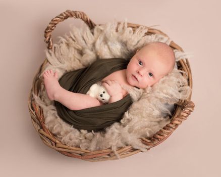 Little cute blue-eyes baby covered in a dark green blanket lying on the soft light brown bedcover