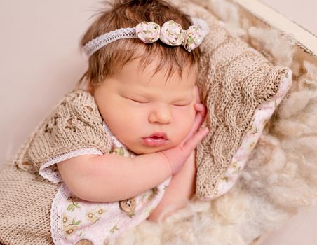 Cute little baby in knitted beanie and skirt sweetly sleeping on the light coverlet