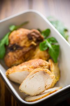 baked chicken fillet pieces with spices and herbs, in a ceramic form on a wooden table