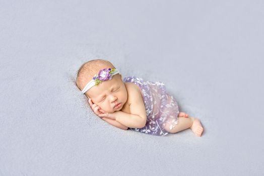 Naked baby girl wearing flowery hairband sleeping on her side, hands pressed to the cheek