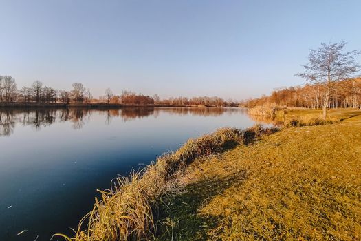 Vivid autumn day. Autumn landscape over river with bright grass on shore. Scenic nature at bright evening with colorful sky and water.