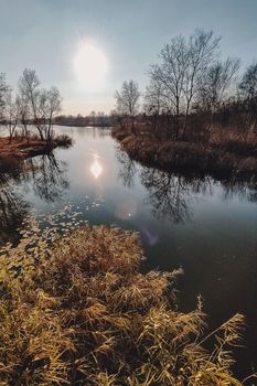 Vivid autumn sunset. Autumn landscape of sunset over river with shining grass on shore. Scenic nature at bright evening with colorful sky.