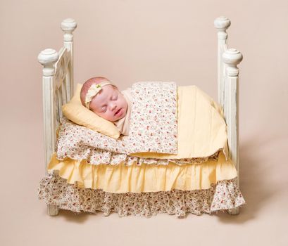 Little cute baby sweetly sleeping in the small white bed covered with light yellow blanket