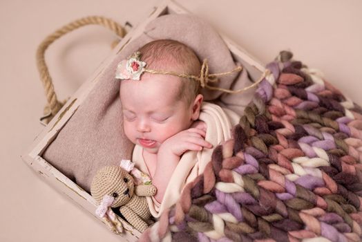 Little cute baby sweetly sleeping on the brown pillow and toy covered with colorful knitted blanket on the light brown background