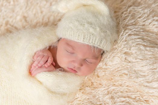Baby napping holding his hands close to his face,wrapped up in a blanket, closeup