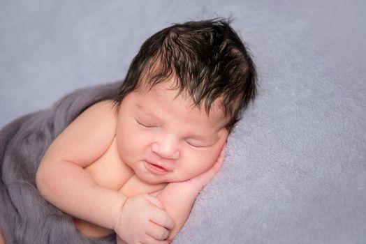 Hairy baby napping on his side, hand under his cheeck, covered with gray blanket, closeup