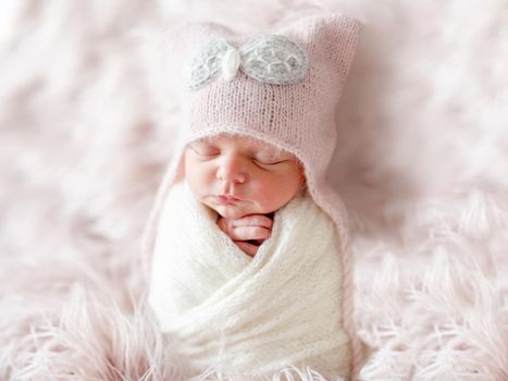 sleepy newborn in a cute beanie hat on a pink shaggy carpet