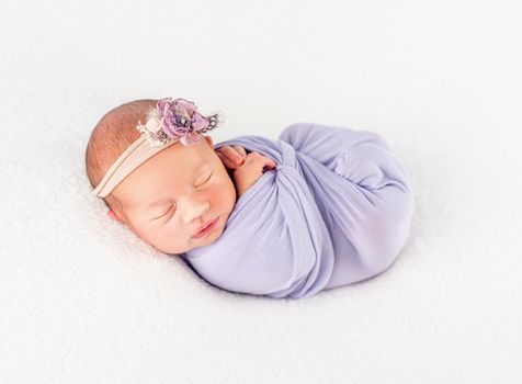 Pretty infant newborn in classy flowery band and blanket, secured with a heart-shaped braid, isolated on white background, closeup