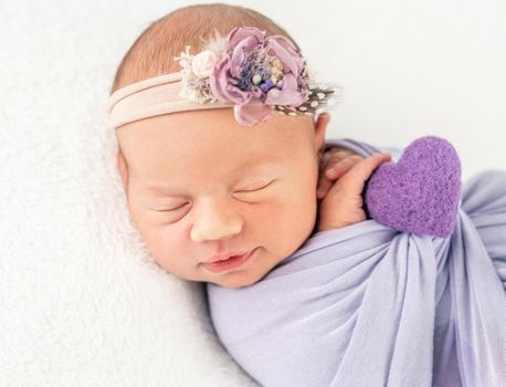 Pretty infant newborn in classy flowery band and blanket, secured with a heart-shaped braid, isolated on white background, closeup