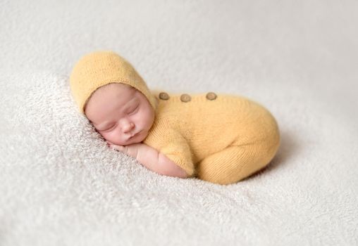 Little baby weared in cute yellow knitted suit sweetly sleeping on the white soft bedcover