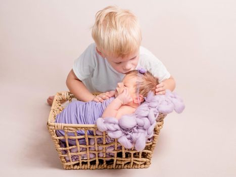 Little blond boy kissing little baby covered in a blue coverlet lying in a basket