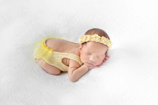 Lovely baby dressed in a yellow outfit with lowcut back sleeping on a white surface