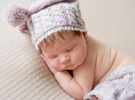 Cute little baby in knitted beanie and skirt sweetly sleeping on the light coverlet