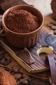 Unsweetened baking block chocolate, cocoa powder, cocoa butter and cocoa beans on old wooden background.