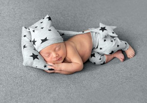 Cute little baby in hat and pants with stars pattern sweetly sleeping on gray blanket