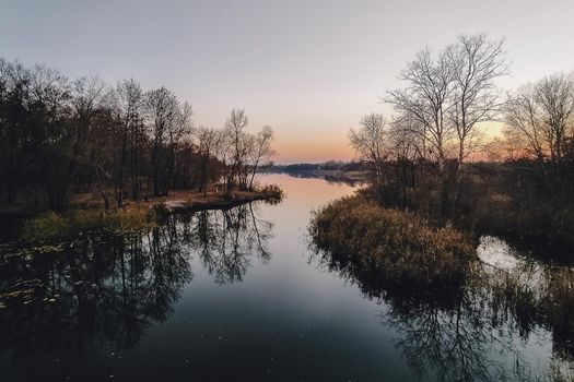 Vivid autumn sunset. Autumn landscape of sunset over river with shining grass on shore. Scenic nature at bright evening with colorful sky.