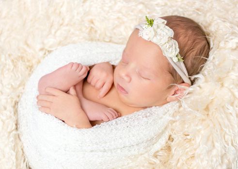 Adorable little girl napping in a nest out of a blanket, wearing a hairband, closeup