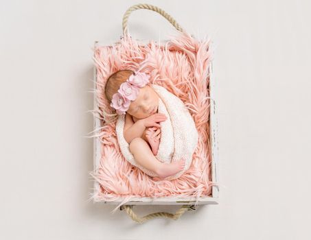 Adorable baby girl wrapped in a white blanket isleeping on a pink soft blanket, topview