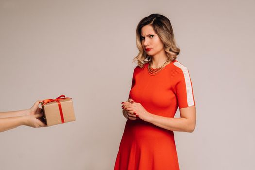A girl in a red dress is given a gift in her hands on a gray background.