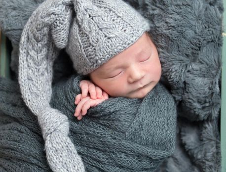 Cute little child sleeping in big knitted gray hat, small hands under his cheek, closeup