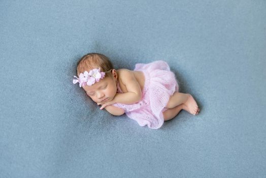 Sweet baby girl sleeping on her tummy, wearing pink little dress, in a flowery hairband