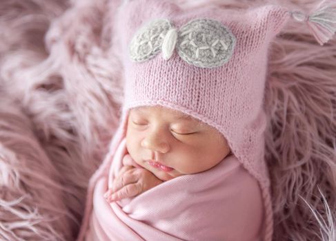 sleepy newborn in a cute beanie hat on a pink shaggy carpet