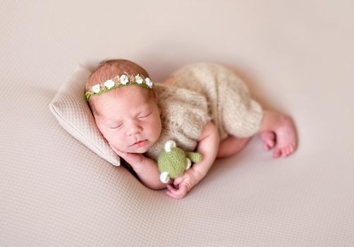 Cute new born child sleeping on pillow with green little toy