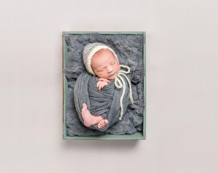 Sweet baby wrapped in a dark gray blanket resting in child's basket, topshot