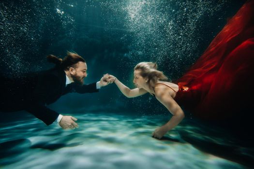 A woman in a red dress and a man in a suit meet under water.A couple of lovers under the water