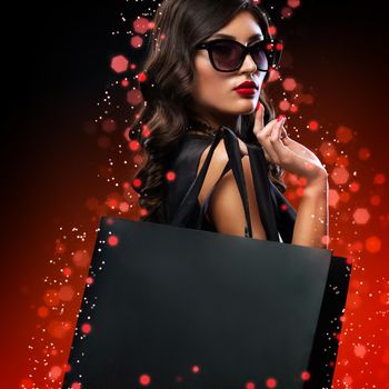 Beautiful young woman make shopping in black friday holiday. Girl with black bag on dark background.