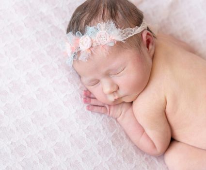 Little nude baby girl speeping on her belly wearing flowery headband, sweet dreams close-up