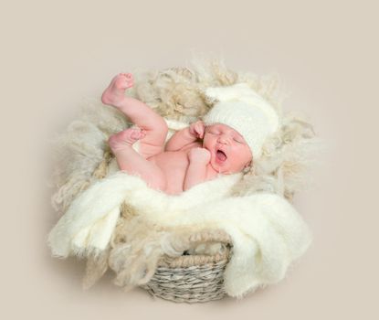 Sweet yawning baby in yellow hat, covered with yellow blanket, lying in a basket