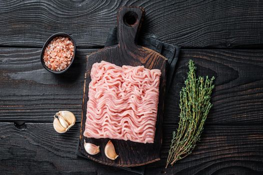 Fresh Raw mince or ground chicken meat on wooden chopping board with thyme. Black wooden background. Top view.