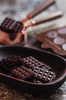 Assortment of different chocolate types in wooden carved plate, with vintage props on the background.