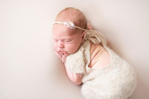 Newborn girl in wool jumpsuit sleeping on light background