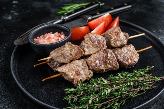 Roasted meat skewers shish kebab and vegetables on a plate. Black background. Top view.