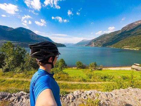 Theme of mountain biking in Scandinavia. human tourist in helmet and sportswear on bicycle in Norway on Hardanger Bridge suspension bridge thrown across the Hardanger Fjord in southwestern Norway.