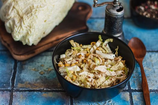 Salad with cabbage, eggs, corns and meat on the plate on rustic tiled table.