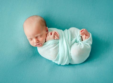 Little newborn wrapped in blue blanket resting in room