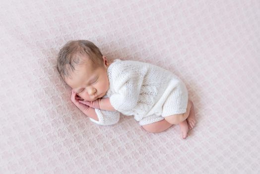 Adorable newborn sleeping on side with his hands under his cheek, dressed in white