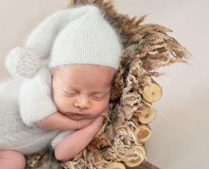 Cute little baby in white hat and knitted suit sweetly sleeping on furry brown pillow