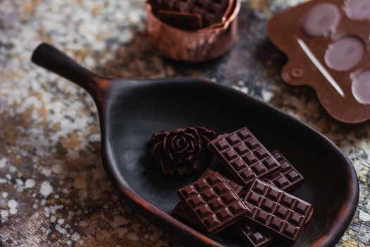 Assortment of different chocolate types in wooden carved plate, with vintage props on the background.