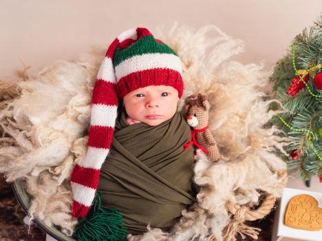 Little baby in big new year hat covered in blanket with toy