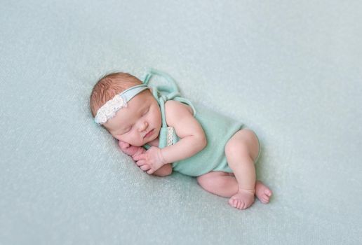 Aborable baby napping oh her side, wearing greenish dress and a flowery hairband