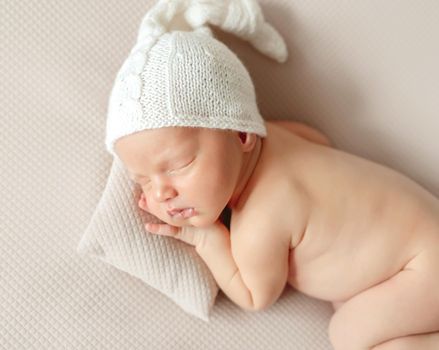 Adorable little baby in knitted hat sleeping on small pillow on cream background