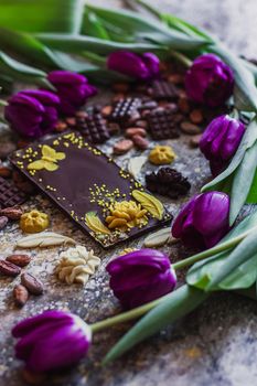 Assortment of different chocolate types in cocoa beans, with violet spring tulips on the background.
